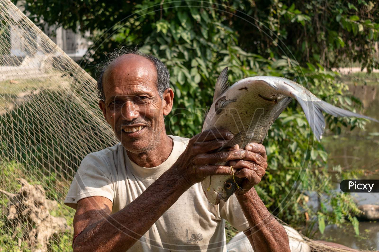A poor fisherman in a village in West Bengal, India, is fishing with nets from the pond