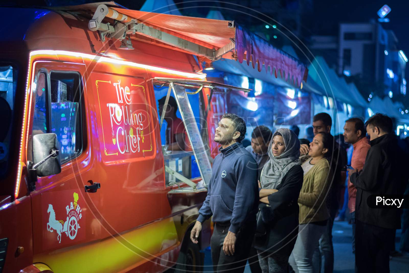 Bangalore, Karnataka / India - August 08 2019: A group of people waiting outside a red food truck for their orders during night time