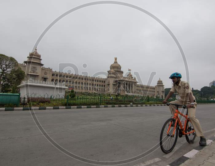 Bengaluru, Karnataka / India - July 26 2019: A policeman on cycle wearing a cycling helmet standing in front of the legislative/administrative building 'Vidhana Soudha' on a cloudy morning