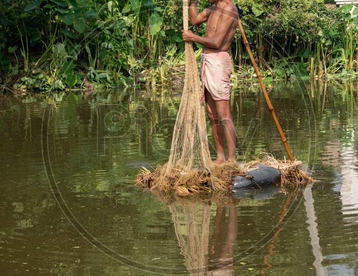 A village fisherman is throwing a net for fishing in a pond