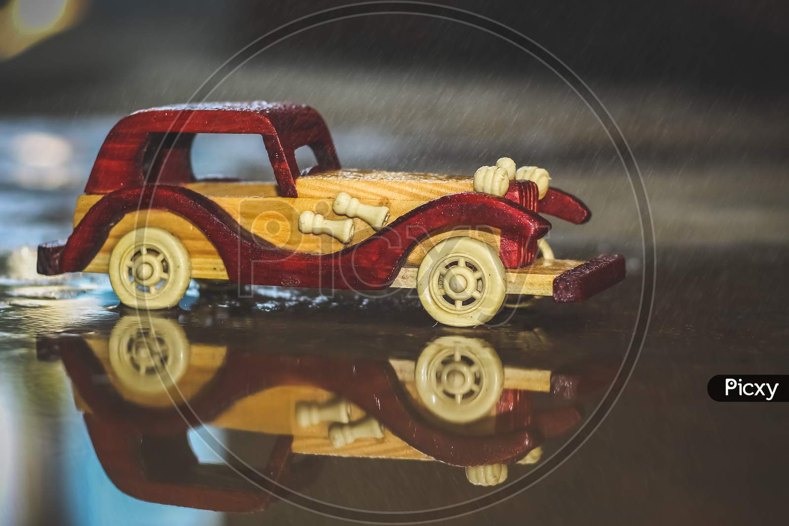 Reflection Vintage Toy Car Under The Rain On The Road. Miniature Car Toy Reflection In Rain. Reflection Red And Yellow Vintage Car On Rain. Rain Falling On Vintage Car Toy Close