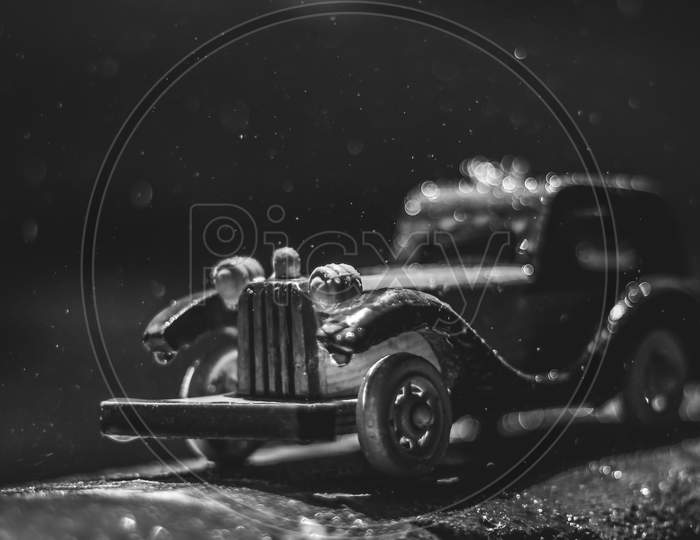 Vintage Toy Car Under The Rain On The Road. Miniature Car Toy In Rain. Red And Yellow Vintage Car On Rain. Rain Falling On Vintage Car Toy Close