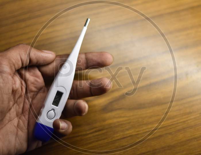 white thermometer in a man hand with a wooden background