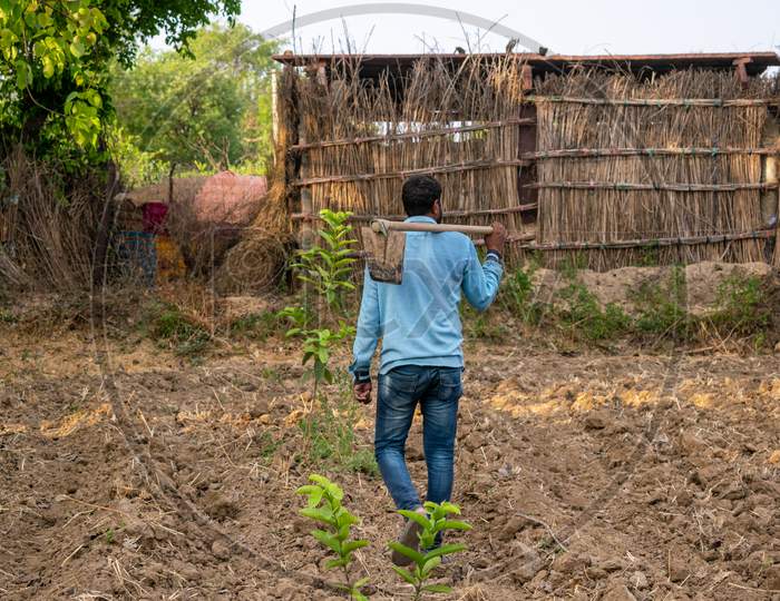 A farmer carries spade on his shoulder as he works at his farm in a village