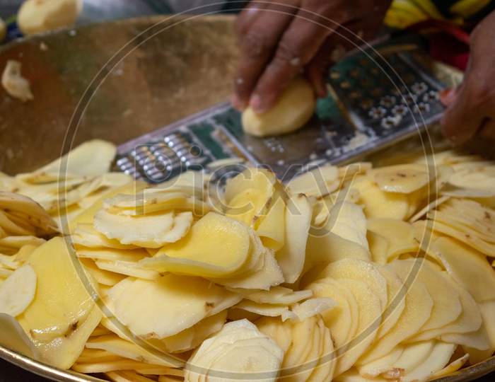 Potato slices are being cut using chips slicer to prepare potato chips