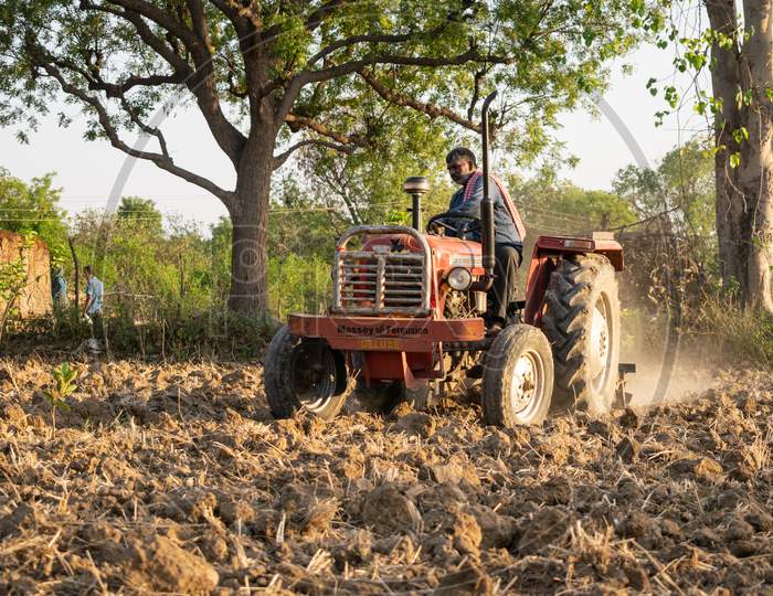 A farmer uses tractor to make soil boundaries at a farm for irrigation purpose in a village