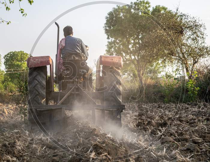 A farmer uses tractor to make soil boundaries at a farm for irrigation purpose in a village