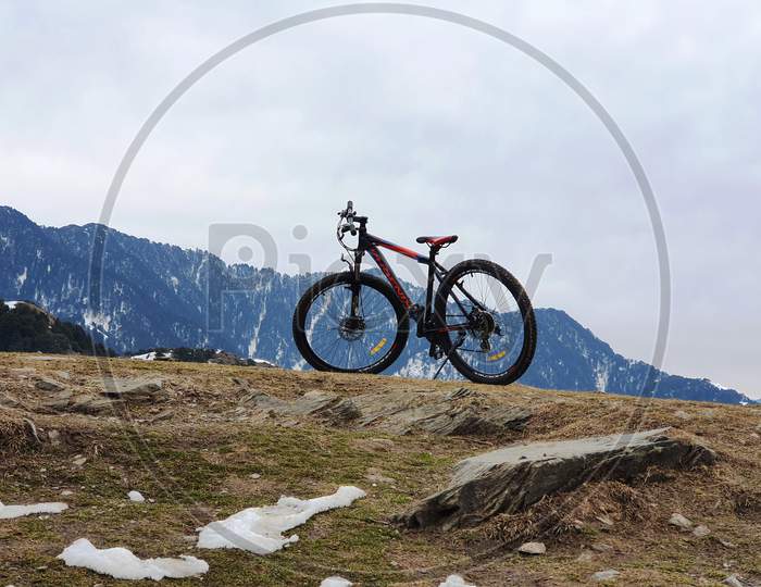 A Bicycle On The Cliff Of a Hill With Mountains in Background In Himachal Pradesh
