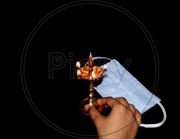 Covid-19, Burning Lamp With Protective Mask In Dark Background, Prayer Symbol For Protection And Blessing With Indian Traditional Culture, Selective Focus With Blur In Night