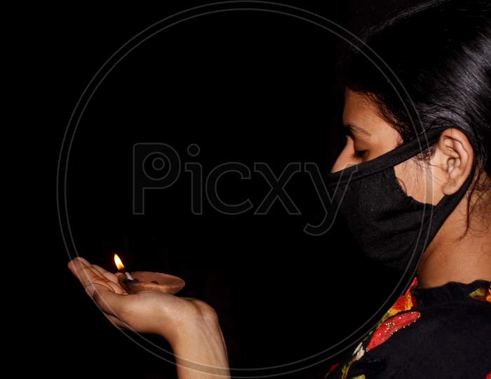 Covid-19 Infected Sad Asian Women Wear Protective Mask And Hand Holding Burning Lamp For Protection And Blessing With Indian Traditional Culture, Selective Focus With Blur In Dark Night Background.