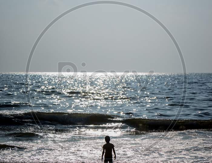 Silhouette Small Boy Playing On The Morning Sunrise. Standing Alone On Beach Waves