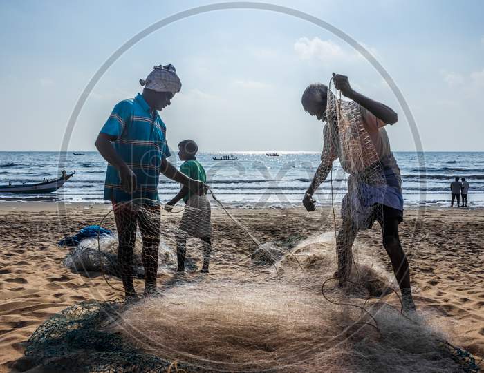Fisherman Taking The Fish From Nylon Fishing Net. Indian Fisherman Working On Their Net On Beach Sand