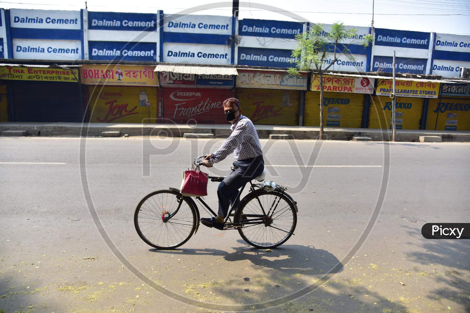 A Man Wearing A Mask Rides A Bicycle  Past Near A Closed Market  During The Nationwide Lockdown In The Wake Of Coronavirus Pandemic In Nagaon District Of Assam,India