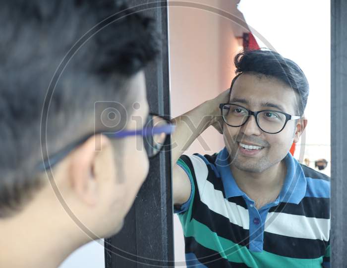 A Man With Eyeglass Looking At His Reflection In Mirror And Smiling At Himself.