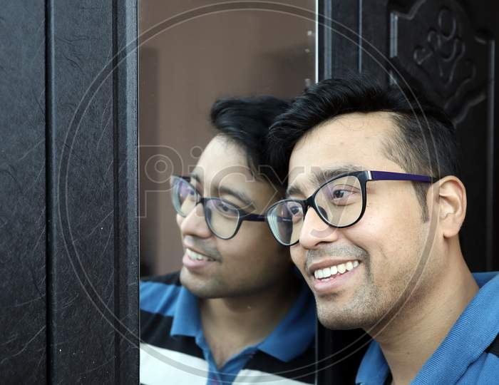 A Man In Eye Glasses And His Reflection In Mirror Smiling In Happy Mood.
