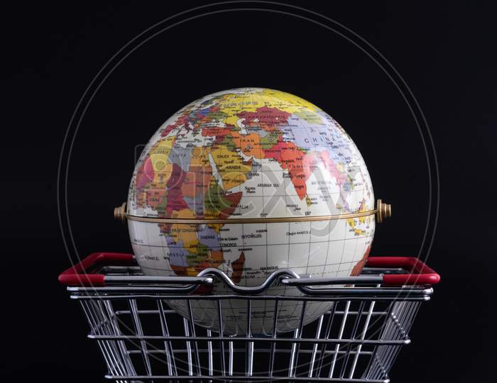 Tiny Metal Shopping Basket And Globe Model Against Black Background