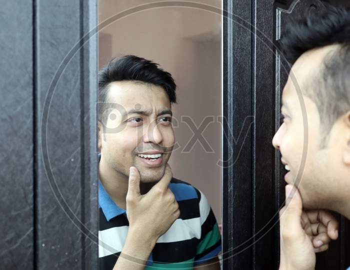 A Man Looking At His Reflection In Mirror And Making Smile Gesture.