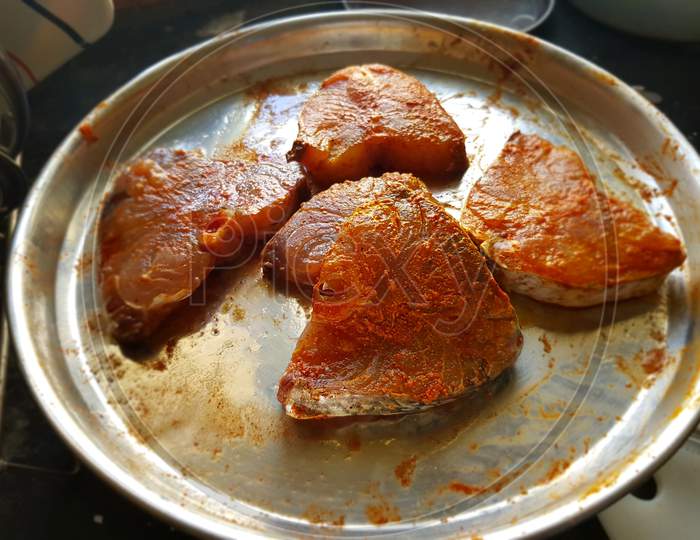 Slices of fishes marinating in spicy curry on a stainless steel plate