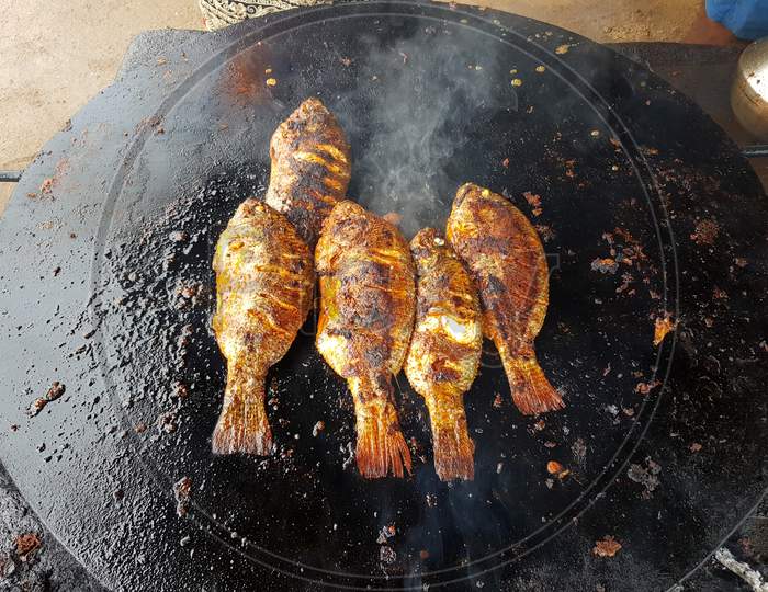 Fishes being fried on a cast iron pan