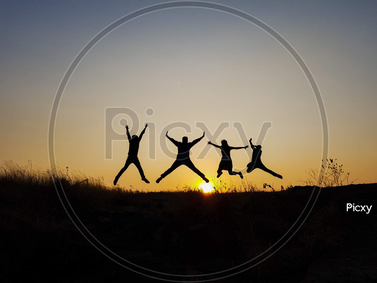 A silhouetted photo of a girl and three boys jumping in the air during sunset