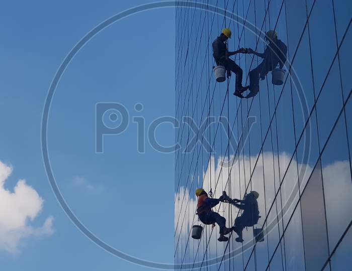 Bengaluru, Karnataka / India - December 09 2019: Medium wide shot of two window washers hanging and cleaning windows of a tall building