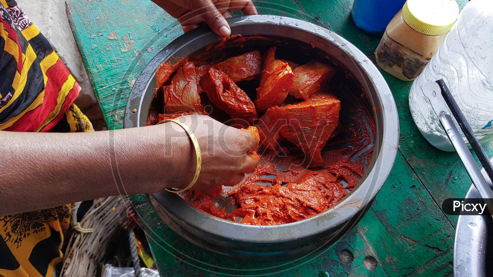A woman wearing bangles marinating sliced fishes in a spicy curry