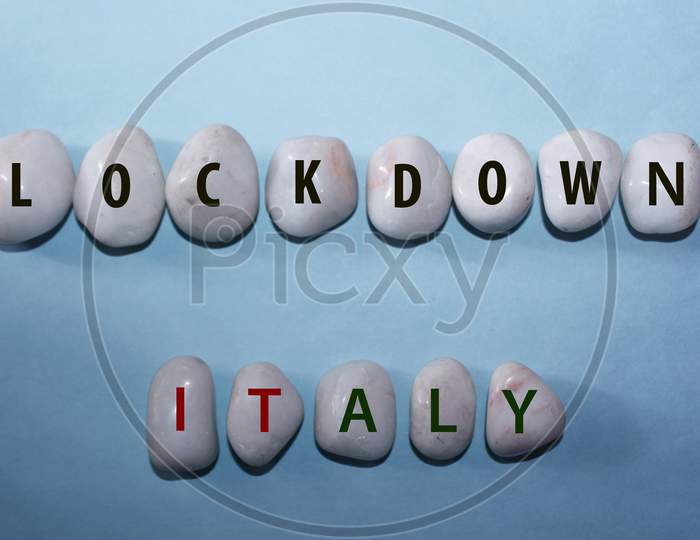 Concept Coronavirus. Lockdown Italy As A Text With Letters On White Royal Sapphire Rock Pebbles, Template Against A Blue Background