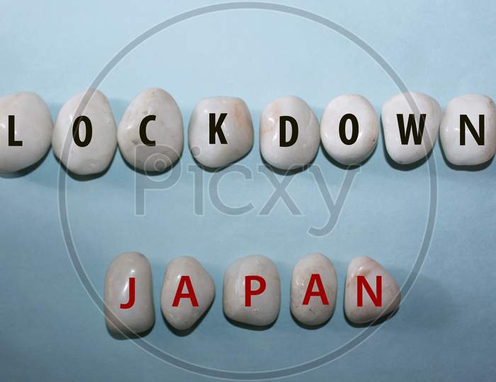 Concept Coronavirus. Lockdown Japan As A Text With Letters On White Royal Sapphire Rock Pebbles, Template Against A Blue Background
