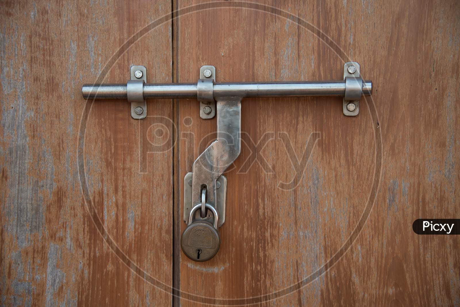 Closeup of a metal latch with a lock on wooden door