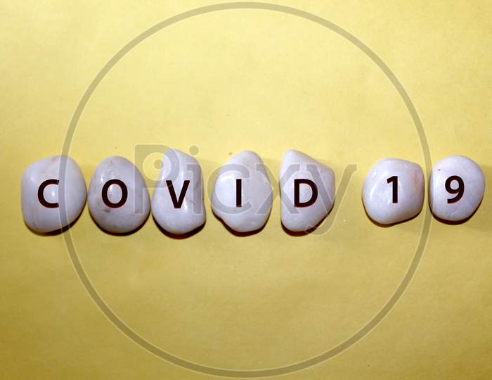 Concept Coronavirus. Covid 19 As A Text With Letters On White Royal Sapphire Rock Pebbles, Template Against A Yellow Background