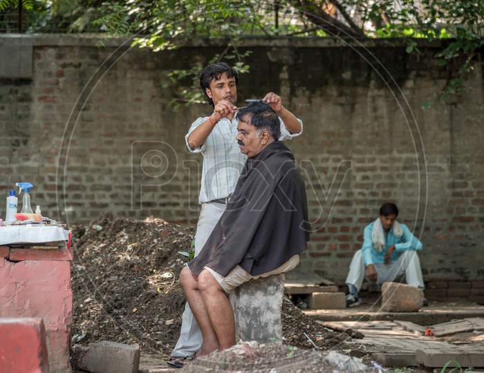 Delhi, India - November 12 2019: A man taking a haircut at a roadside barber shop in the morning
