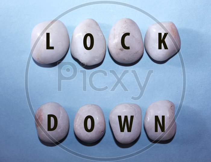 Concept Coronavirus. Lock Down As A Text With Letters On White Royal Sapphire Rock Pebbles, Template Against A Blue Background
