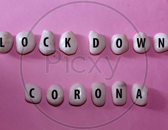 Concept Corona Virus. Lock Down Corona As A Text With Letters On White Royal Sapphire Rock Pebbles, Template Against A Pink Background