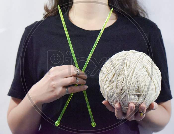 Knitting Needles And The Ball Of Yarn In Hands Of Woman In Black On The White Background. Concept Of Handmade Crafts.