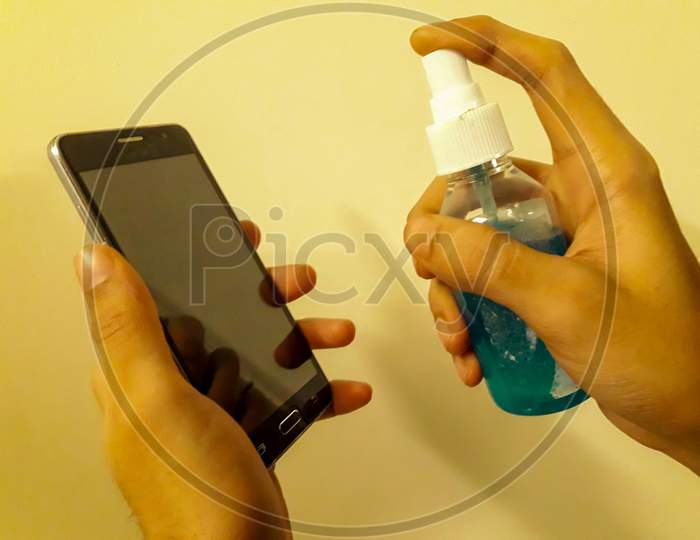 Disinfecting The mobile phone With Sanitizer to avoid the spread of COVID 19 or coronavirus With orange Background