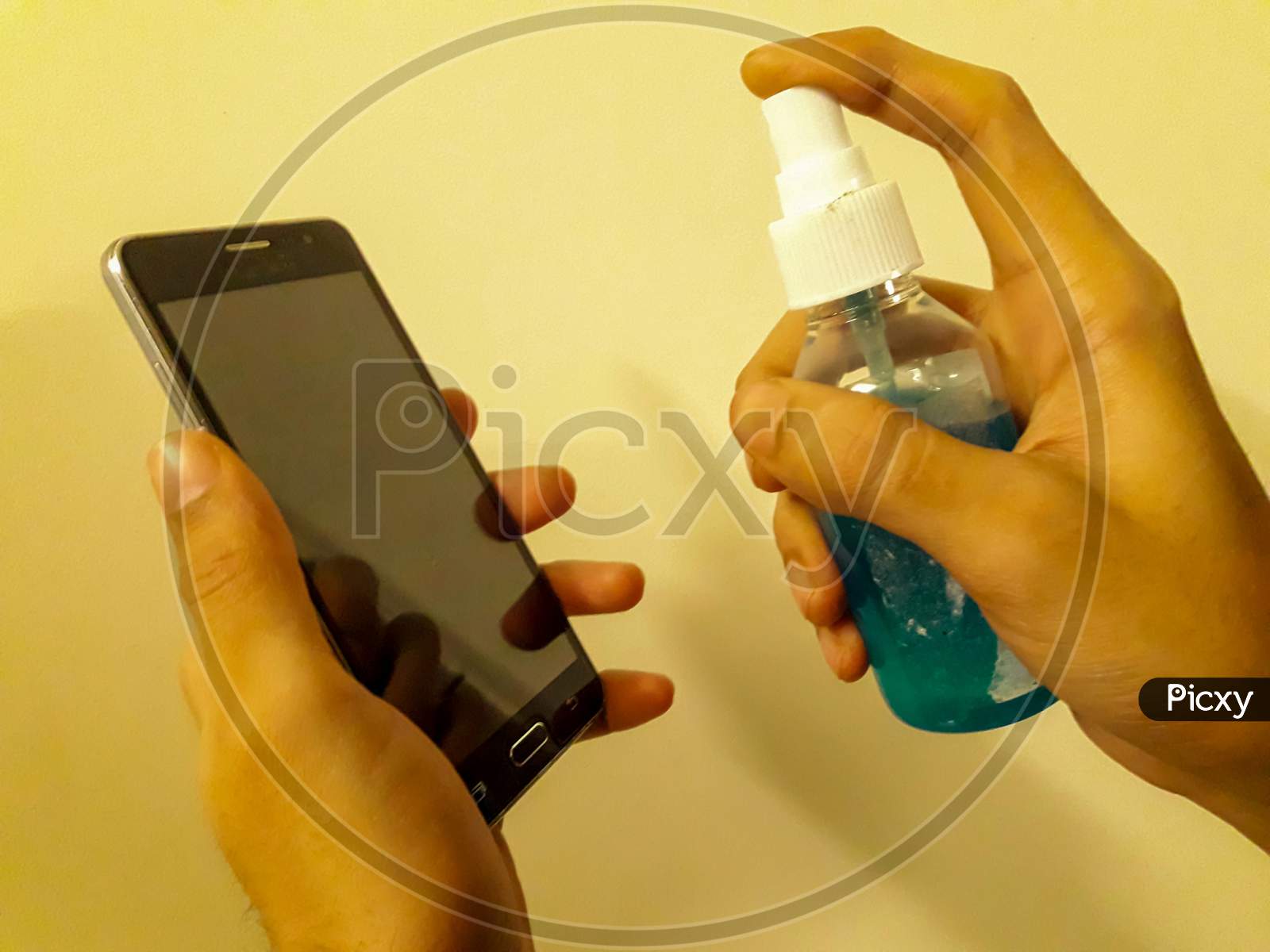 Disinfecting The mobile phone With Sanitizer to avoid the spread of COVID 19 or coronavirus With orange Background