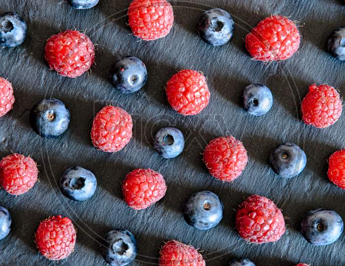lines of raspberry and blueberry arranged in pattern on black conceptual photo