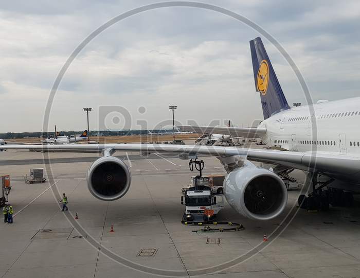 An airbus A380 aircraft getting parked at the terminal in Frankfurt airport during day time and maintenance personnel walking on the tarmac