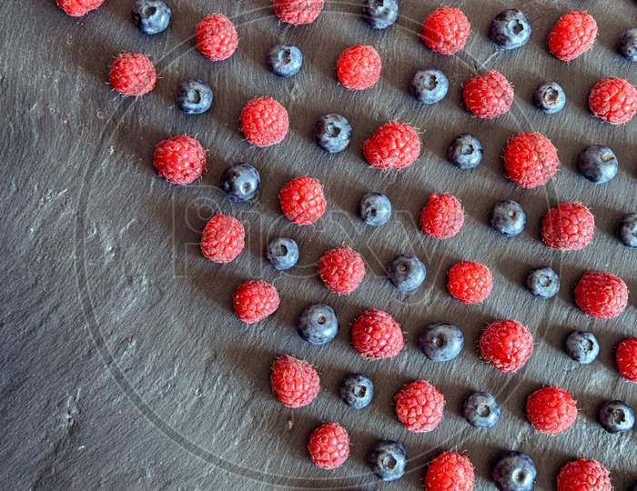 lines of raspberry and blueberry arranged in pattern on black conceptual photo