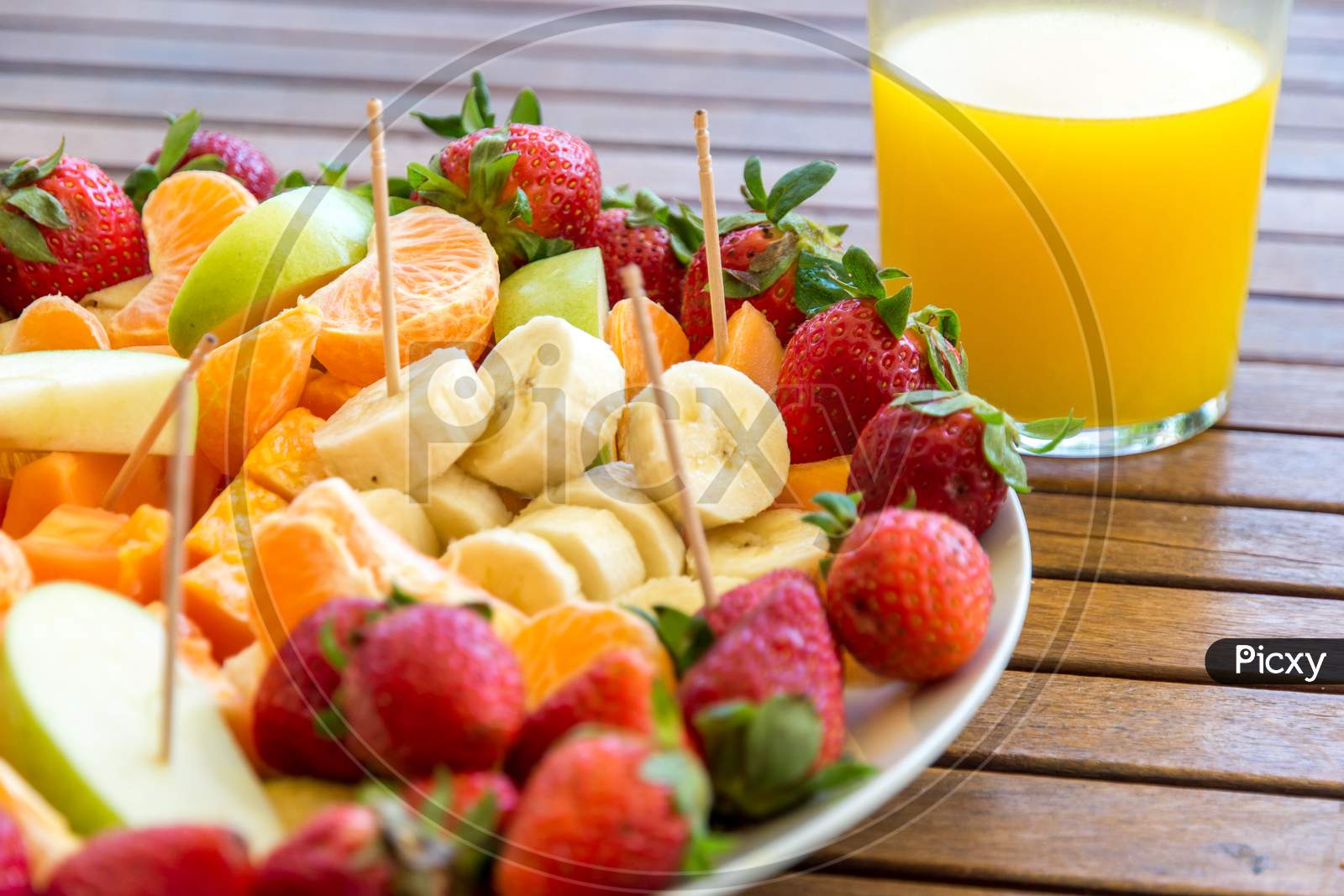 plate with assortment of fruit slices on a wooden table and glass with fresh orange juice healthy eating concept
