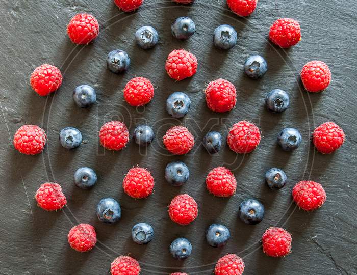 raspberries and blueberries arranged in a pattern of concentric circles with copy space