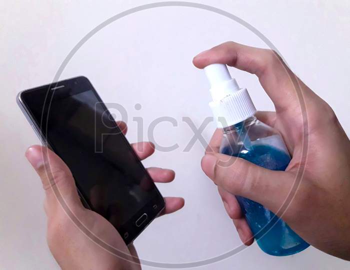 Disinfecting The cellphone with Sanitizer to avoid the spread of COVID 19 or coronavirus With white Background