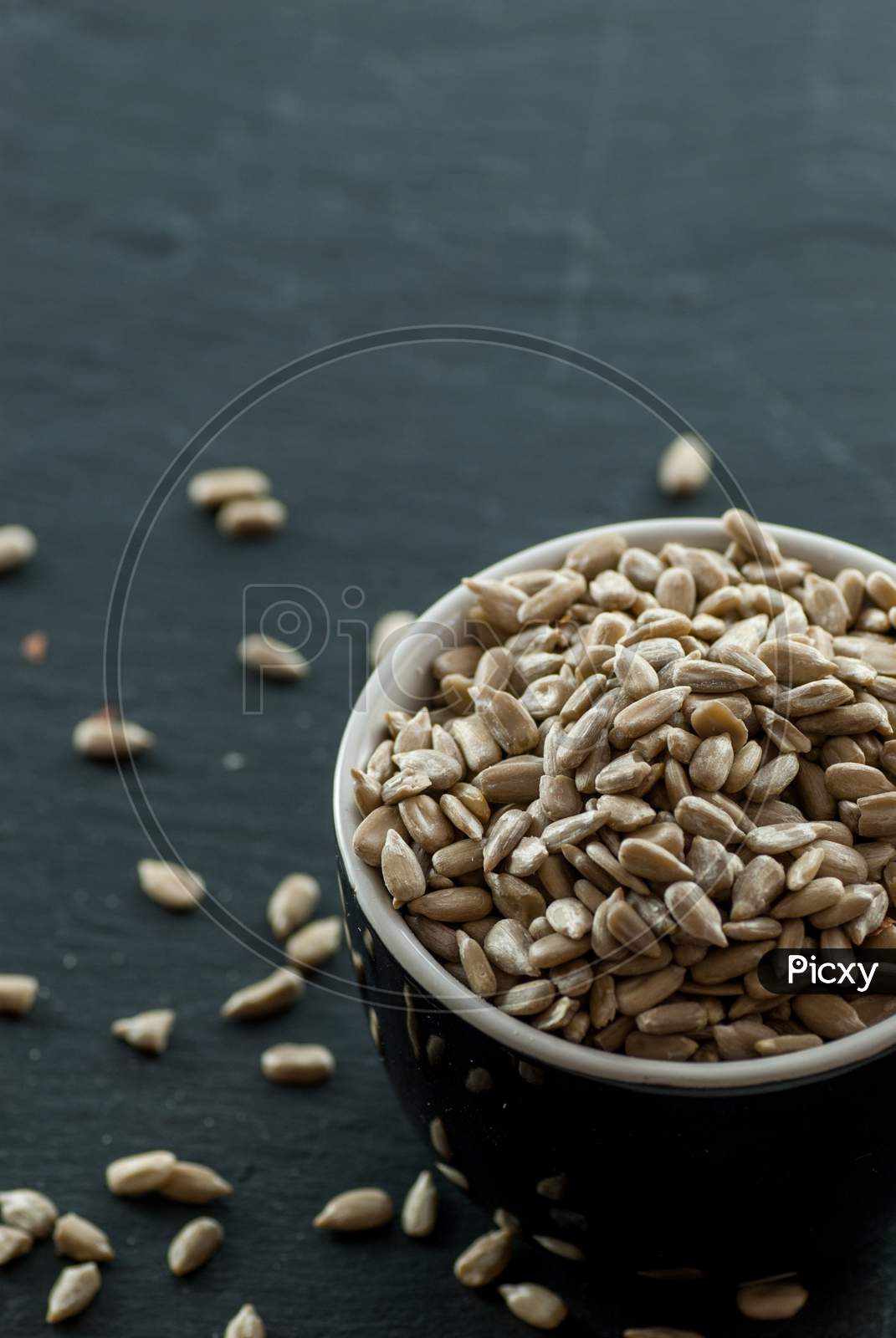 bowl with raw sunflower kernels and kernels spread around on a slate plate with copy space
