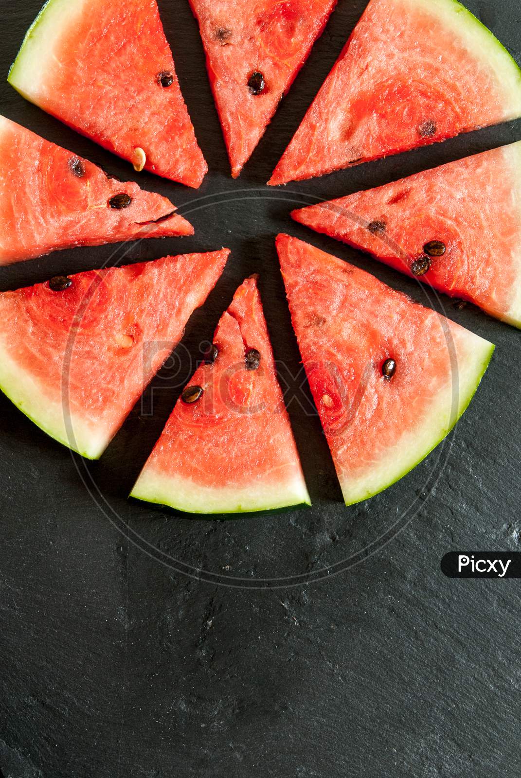 pieces of water melon arranged in circle on black with copy space