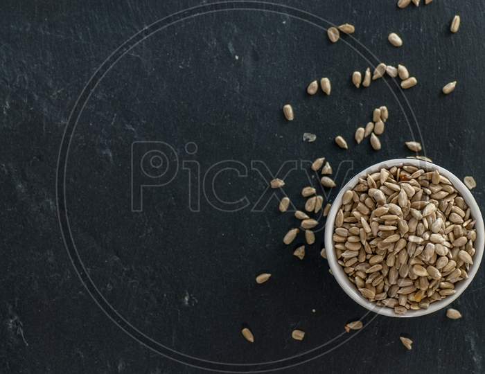 bowl with raw sunflower kernels and kernels spread around on a slate plate with copy space
