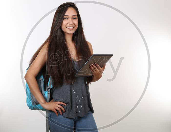 An Attractive College Student Smiles At The Camera As She Holds Her Tablet And Listens To Music.