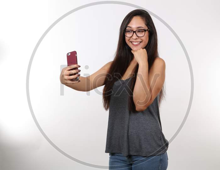 An Attractive Female Wearing Glasses In Casual Clothes Takes A Selfie On Her Phone.