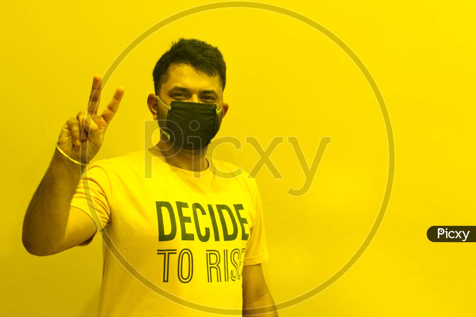 Indian guy wearing mask with victory sign to stop covid spread with yellow background and open Space for text