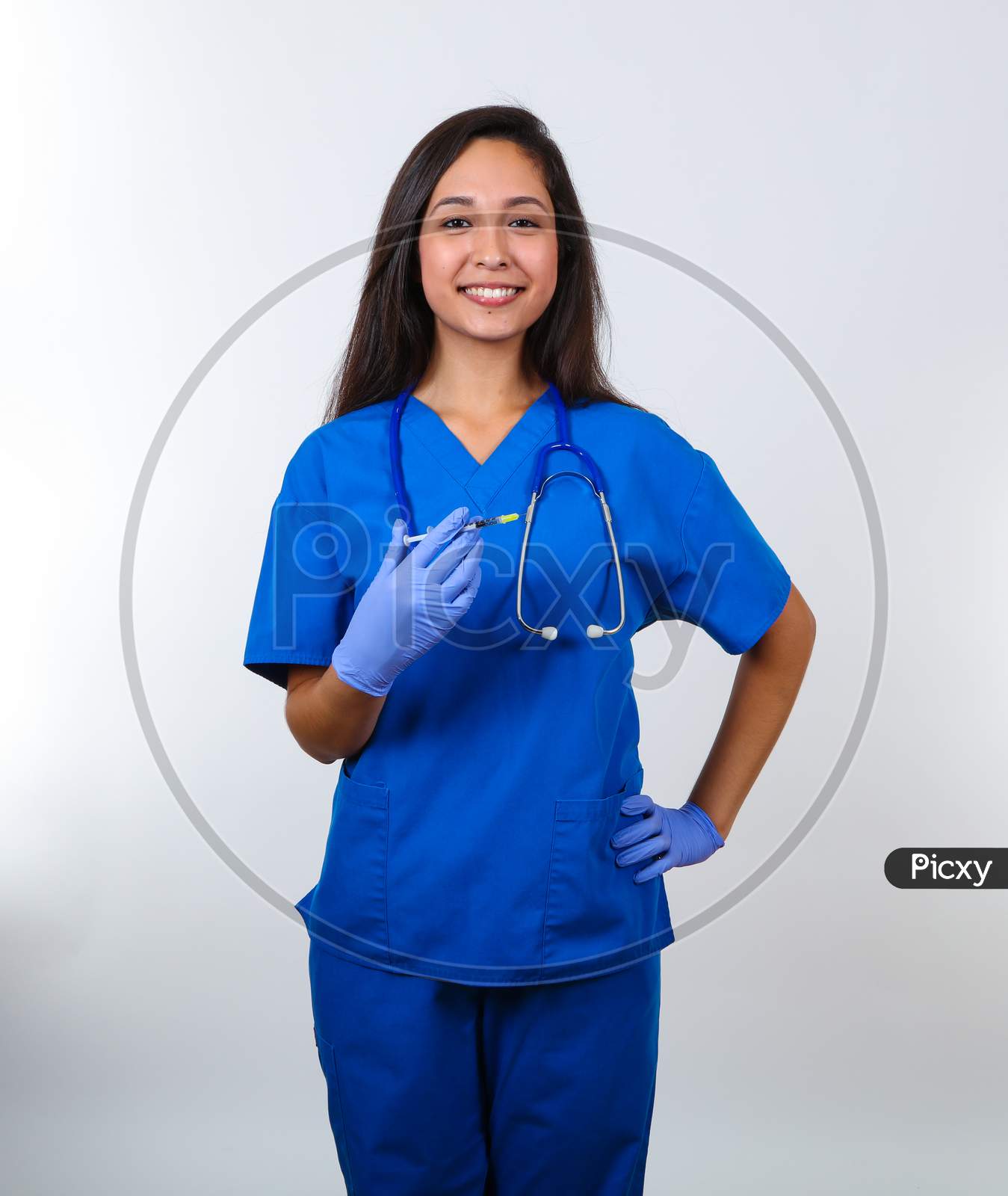 An Attractive Nurse In Blue Scrubs Proudly Holds A Vaccine.