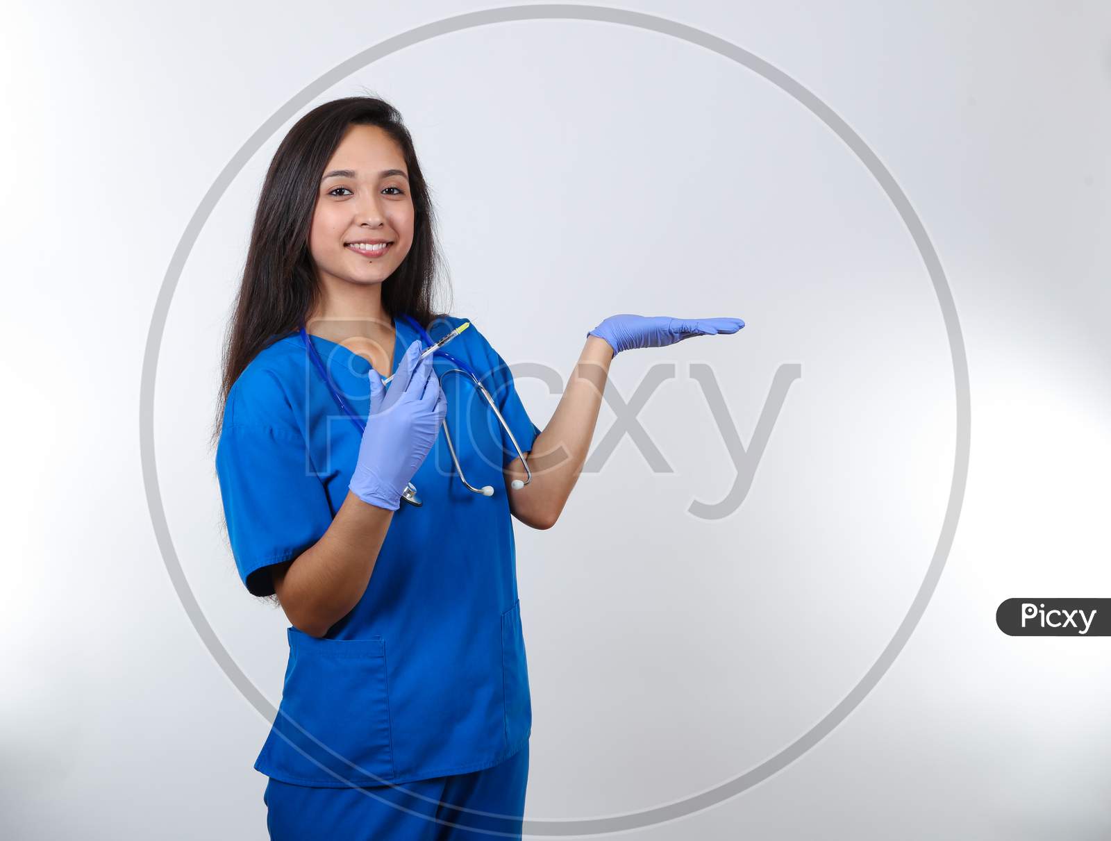 An Energetic Nurse In Scrubs Holds A Syringe And Her Hand Up.